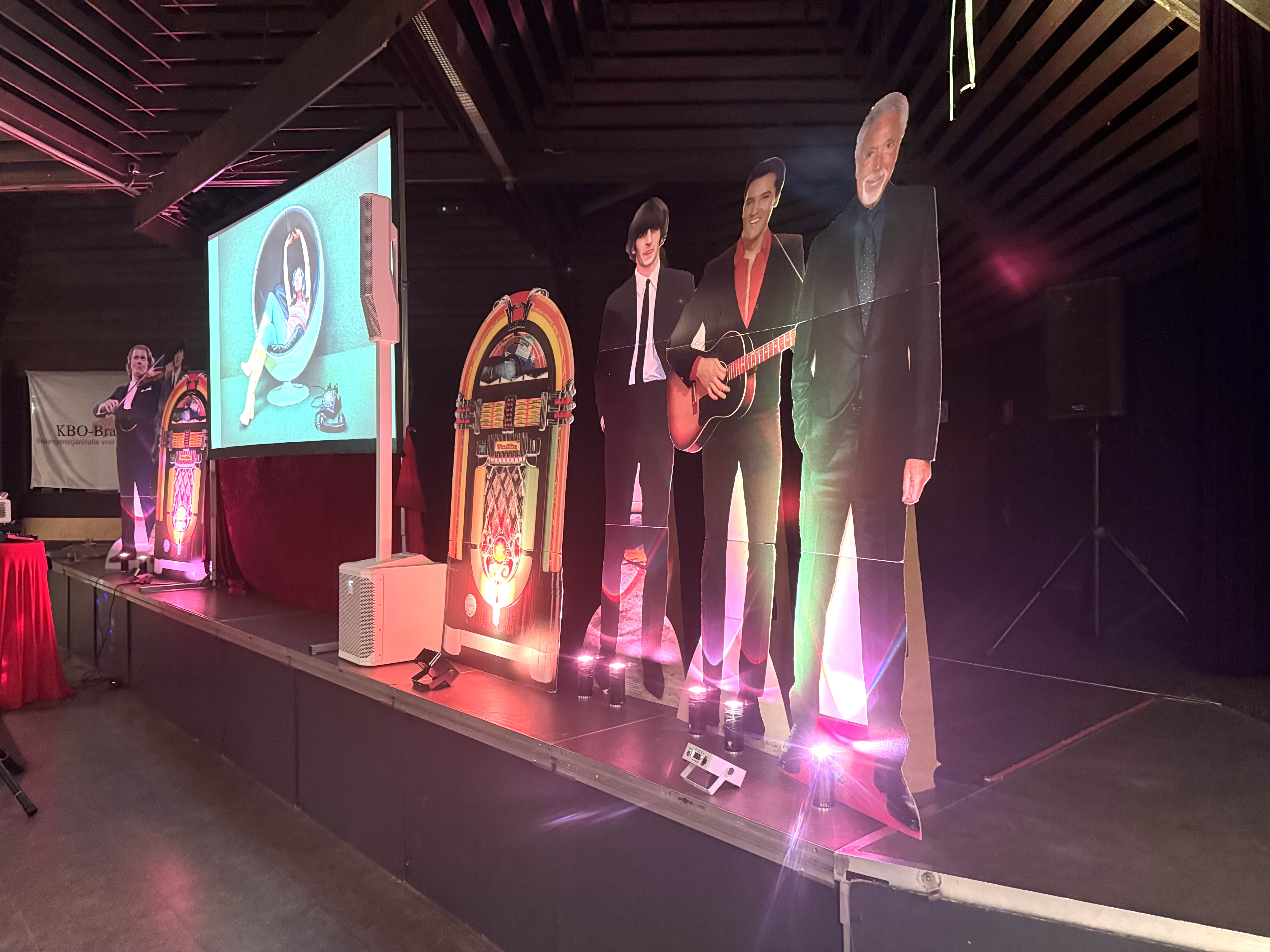 Levensechte kartonnen sterrenfiguren met jukeboxen en verlichting als decor bij muziekoptreden voor ouderen